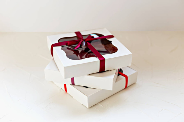 Tres cajas de papel blanco con caramelos uno encima del otro sobre fondo claro. Pastelería hecha a mano. Bonitos regalos dulces - Foto, imagen