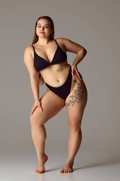 Full length portrait of young chubby woman posing in lingerie against grey studio background. Self-expression. Concept of natural beauty, femininity, body positivity, dieting, fitness, lose-weight. - Photo, Image
