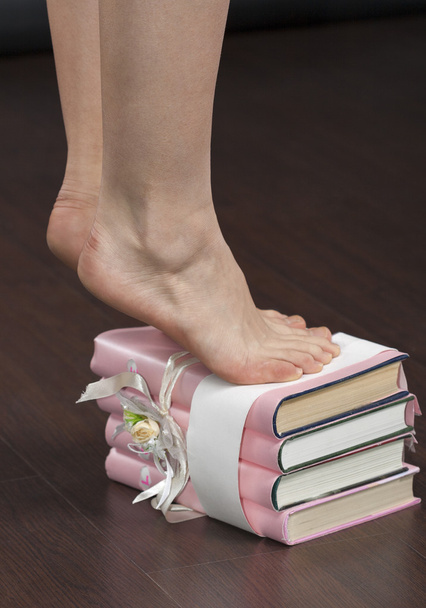 Καυκάσιος γυναίκα πόδια μόνιμης κάνουν πολλά μικρά βήματα στη στοίβα από βιβλία closeup - Φωτογραφία, εικόνα