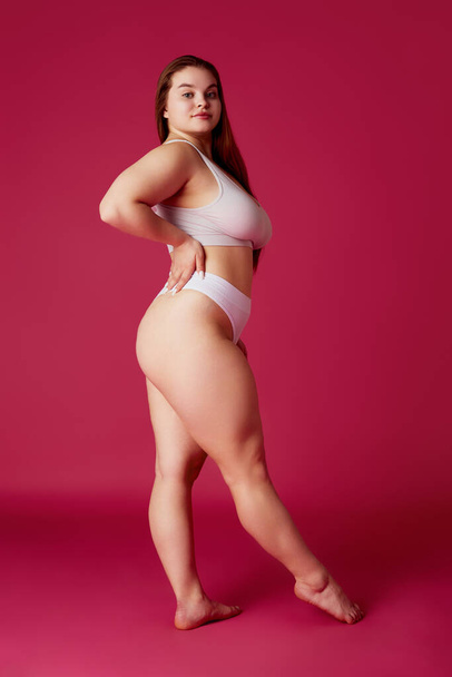 Young attractive, confident woman posing in while lingerie, bikini looking away against vibrant pink studio background. Concept of natural beauty, femininity, body positivity, dieting, fitness. - Photo, Image