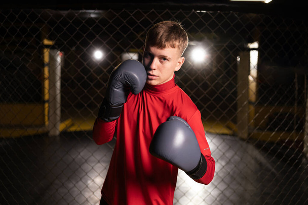 Retrato de un joven boxeador con guantes realizando un puñetazo mientras mira a la cámara. Artes marciales y concepto deportivo - Foto, imagen