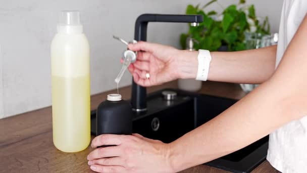 Nainen kaataa saippuaa tai pesuainetta kierrätyspakkauksesta uudelleen käytettävään pulloon keittiössä. Ympäristöystävällinen elämäntapa käsite. Laadukas 4k kuvamateriaalia - Materiaali, video