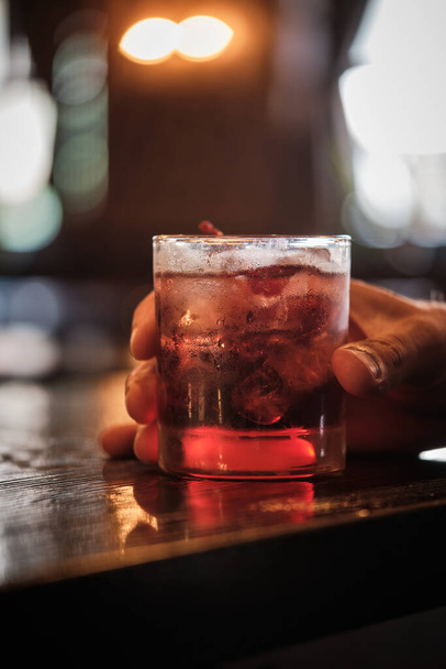 Un'immagine ravvicinata che cattura un momento di qualcuno che regge un bicchiere di cocktail di ciliegie, guarnito con una ciliegia, in un bar ben illuminato. - Foto, immagini
