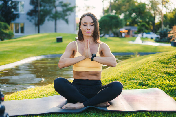 Mooie jonge vrouw in meditatieve houding op yoga mat met haar ogen dicht in gebed pose. Yoga bij natuurconcept. Meisje met gebedshanden. - Foto, afbeelding