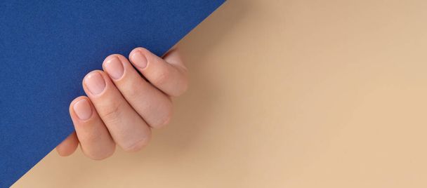 Vrouw gemanicuurde handen, stijlvolle beige nagels. Close-up van gemanicuurde nagels van vrouwelijke hand in blauwe trui in blauwe achtergrond. Mock up template kopieerruimte Winter of herfst stijl van nagel ontwerp concept. Schoonheidsbehandeling. - Foto, afbeelding