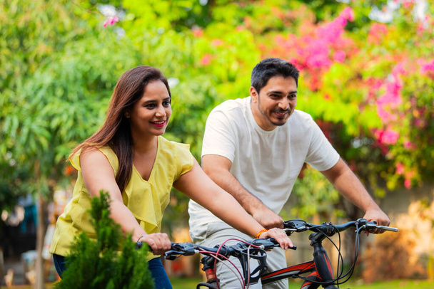 Indian young Couple on bikes or bicycle outdoors smiling - Photo, Image