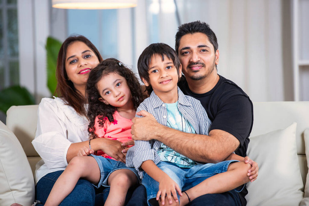 Muotokuva Happy intialainen nuori perhe neljän istuu sohvalla olohuoneessa - Valokuva, kuva