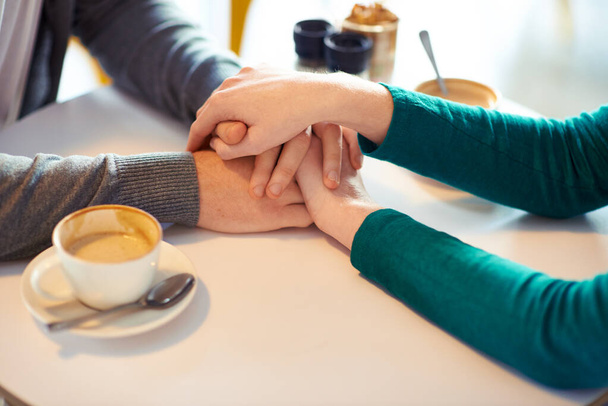 Trzymanie się za ręce, para i kawa w kawiarni z miłością, romansem i uczuciem w rocznicę ślubu. Szacunek, wraz z troską i więzią, lojalnością i wsparciem w związku z cappuccino dla ludzi. - Zdjęcie, obraz