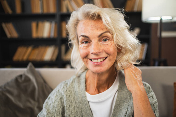 Портрет уверенной стильной европейской пожилой женщины. Пожилая женщина 60-х годов улыбается дома. Счастливая привлекательная пожилая женщина смотрит крупным планом на портрет. Счастливые люди - Фото, изображение