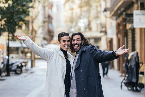 Glückliches homosexuelles Paar lächelt und macht lustige Gesichter, während es draußen auf der Straße posiert. Lgbt-Konzept. - Foto, Bild