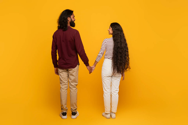 Eine Rückansicht eines Mannes und einer Frau, die Hand in Hand gehen, der gelbe Hintergrund weckt Wärme und Optimismus für zukünftige Wege. - Foto, Bild