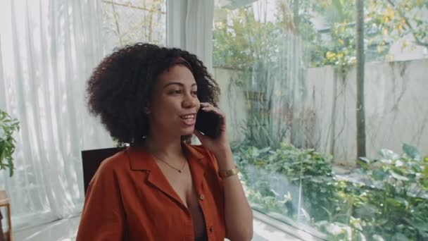 Średnie ujęcie pięknej kobiety pracującej na własny rachunek rozmawiającej z kolegami przez telefon komórkowy i pijącej herbatę w domu - Materiał filmowy, wideo