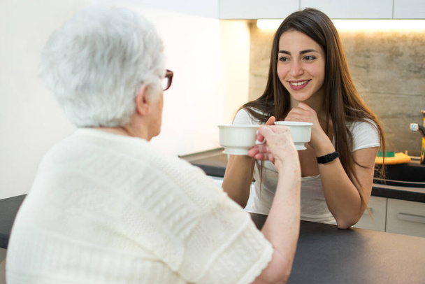 Vnučka si dává šálek kávy s babičkou v kuchyni. - Fotografie, Obrázek