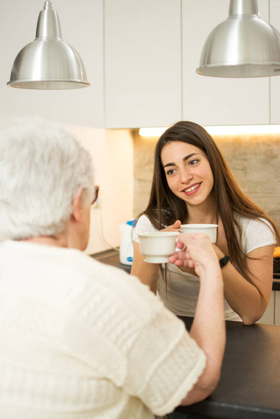 Petite-fille prenant une tasse de thé avec sa grand-mère dans la cuisine. - Photo, image