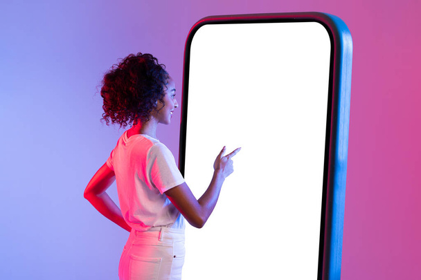 Una señora de blanco se para frente a una gigantesca pantalla de teléfono inteligente en blanco, que representa las tecnologías a gran escala en nuestras vidas - Foto, Imagen