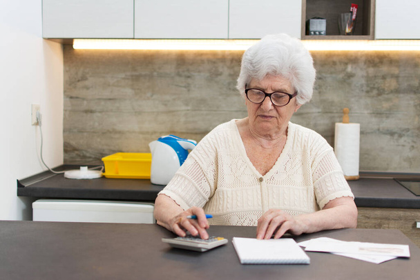 Vanhempi nainen laskimen ja paperit laskenta kotona. - Valokuva, kuva