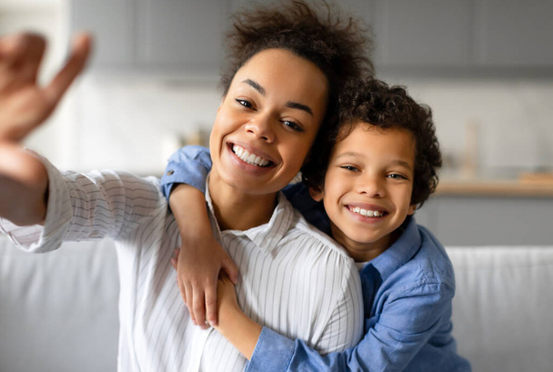 Lächelnde Frau und Kind posieren für ein fröhliches Selfie in einem gut beleuchteten Wohnzimmer - Foto, Bild
