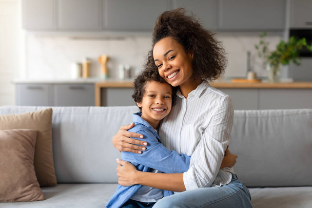 Een liefhebbende Afro-Amerikaanse moeder omarmt haar jonge zoon in een gezellige thuisomgeving - Foto, afbeelding