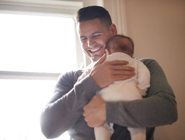 Father, baby and bonding with happiness and hug, growth and child development with love at family home. Man, infant or newborn with smile and dad holding kid for comfort, childhood and parenting. - Photo, Image