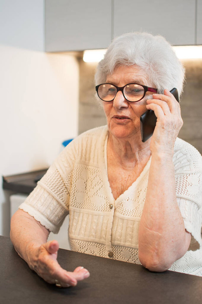 Ευτυχισμένη ηλικιωμένη γυναίκα που μιλάει στο κινητό στο σπίτι. - Φωτογραφία, εικόνα