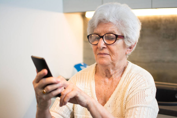 Gelukkig senior vrouw met behulp van smartphone thuis. - Foto, afbeelding