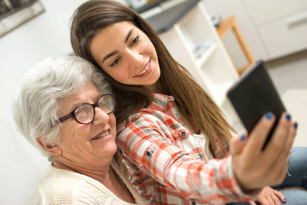 anciana haciendo selfie con su joven nieta en casa
. - Foto, Imagen