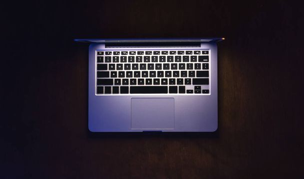 Vue du dessus d'un ordinateur portable sur une table sombre, écran lumineux. Lieu de travail minimaliste, travail avec ordinateur, utilisation d'un ordinateur portable la nuit et concept de confidentialité en ligne. - Photo, image