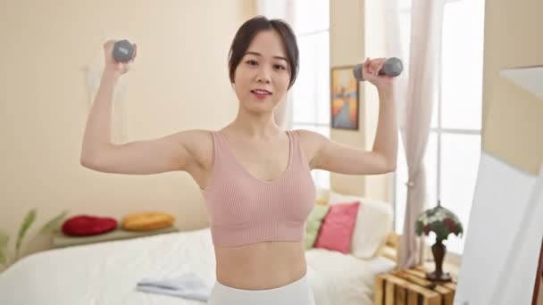 Aasialainen nainen käyttää käsipainoja valoisassa makuuhuoneessa, mikä heijastaa terveellistä elämäntapaa ja sisätilojen kuntoa - Materiaali, video