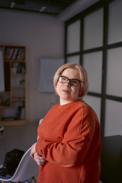 ritratto di una donna con disabilità in un maglione arancione e pantaloni di pelle in ufficio                - Foto, immagini