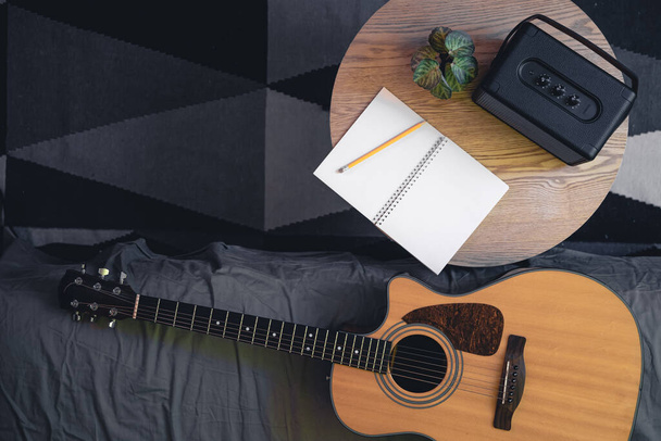 Muzikale achtergrond met akoestische gitaar, luidspreker en notitieblok op tafel, bovenaanzicht. Plaats voor tekst. - Foto, afbeelding