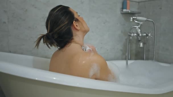 Una joven relajada con el pelo mojado y la piel cubierta de espuma disfruta de un baño tranquilo en un moderno baño de mármol. - Imágenes, Vídeo