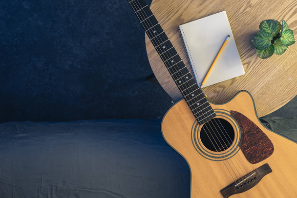Akoestische gitaar en notitieblok met potlood op tafel, bovenaanzicht. Muzikale achtergrond, concept van repetitie, leren gitaar spelen. Kopieerruimte. - Foto, afbeelding