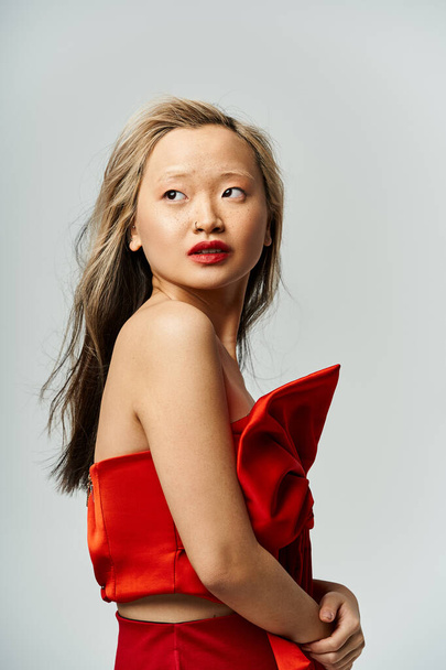An attractive Asian woman in a vibrant red dress strikes a pose for the camera. - Photo, Image