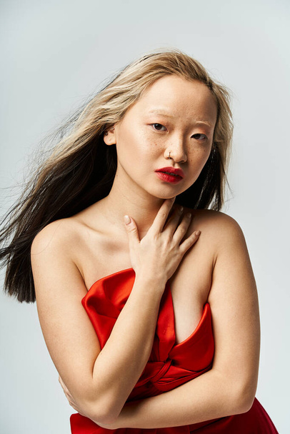 Яскрава азіатська жінка виділяє елегантність у живій позі в червоній сукні. - Фото, зображення