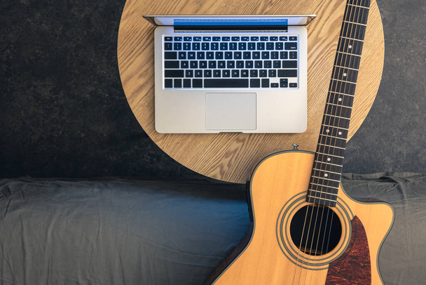 Gitara akustyczna i laptop na drewnianym stole, widok z góry. Muzyka i technologia, cyfrowa koncepcja. Lekcje gry na gitarze. - Zdjęcie, obraz