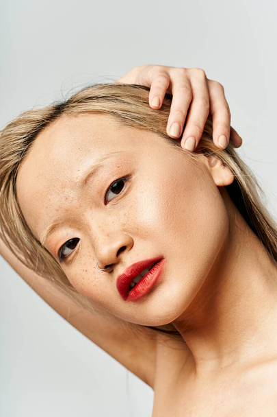 Atraktivní asijská žena v pulzujícím oblečení, chlubící se červenou rtěnkou na tváři. - Fotografie, Obrázek