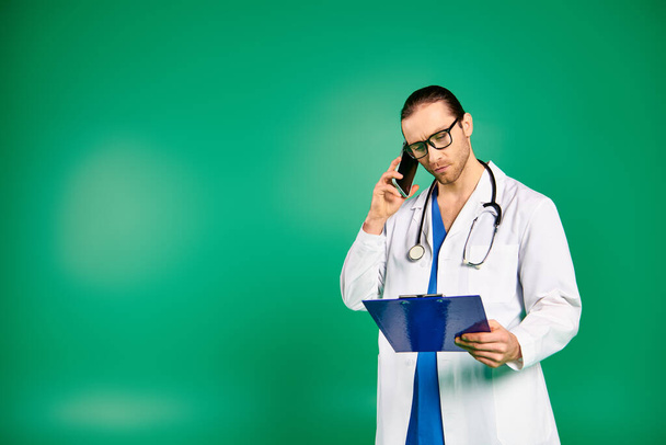 Arzt im weißen Gewand telefoniert, Klemmbrett vor grünem Hintergrund. - Foto, Bild