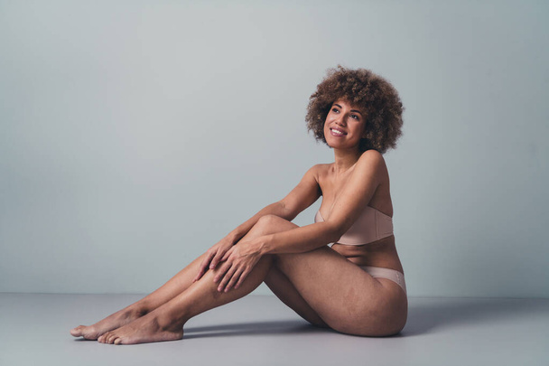 Unretouched photo of body positive girl touch legs smiling after depilation treatment isolated grey color background. - Φωτογραφία, εικόνα
