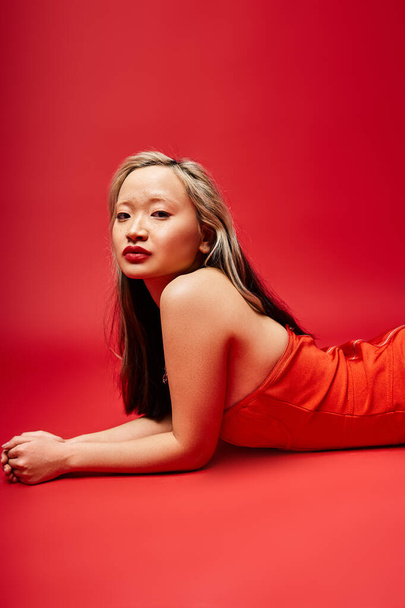 Una donna asiatica attraente in un abito rosso vibrante sdraiata con grazia a terra. - Foto, immagini