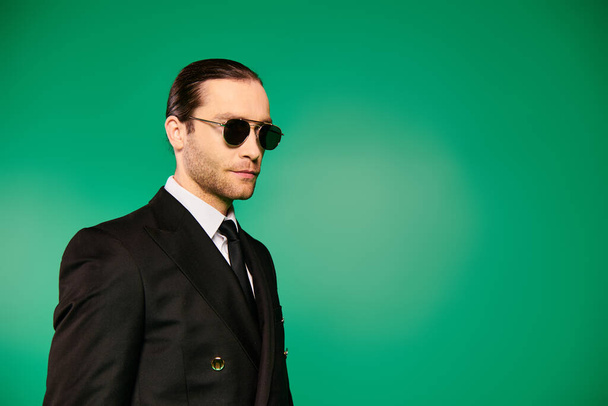 Schöner Pilot in schwarzem Anzug und Sonnenbrille posiert vor leuchtend grünem Hintergrund. - Foto, Bild