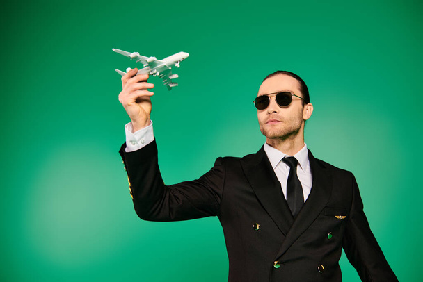Piloto guapo en traje negro sosteniendo avión modelo contra fondo verde. - Foto, imagen
