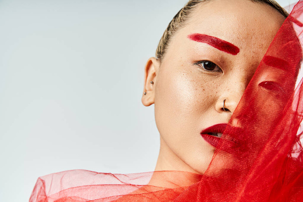 Asijská žena s nápadným červeným make-upem a tekoucím červeným závojem představuje elegantně. - Fotografie, Obrázek
