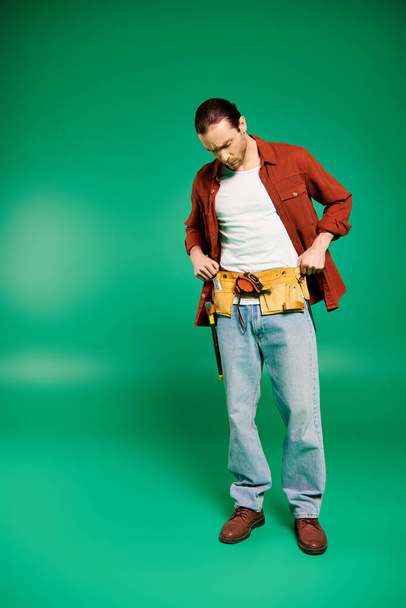 Ένας άντρας με στολή στέκεται με αυτοπεποίθηση κρατώντας εργαλεία σε ένα καταπράσινο φόντο. - Φωτογραφία, εικόνα