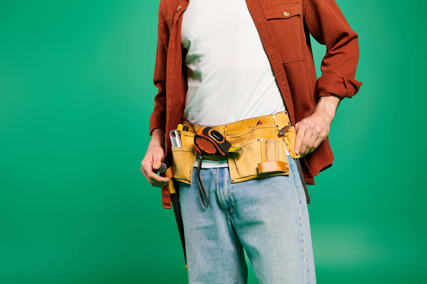 Un homme dans une ceinture d'outils pose sur un fond vert vibrant. - Photo, image