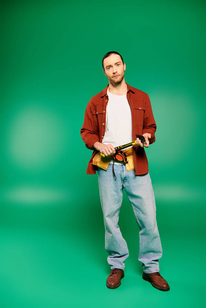 Όμορφος άνδρας εργάτης με στολή με εργαλεία που θέτουν σε πράσινο φόντο. - Φωτογραφία, εικόνα