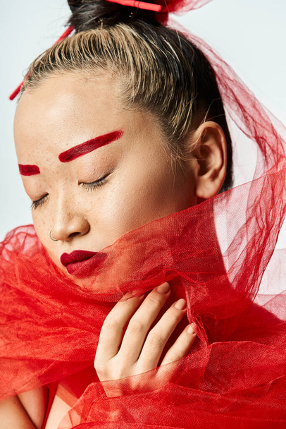 Femme asiatique avec un maquillage rouge audacieux et un voile de tête posant élégamment. - Photo, image