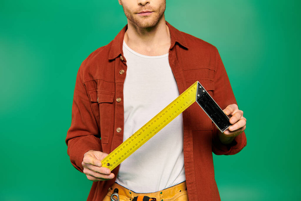 Красивый мужчина в форме держит измерительную ленту на зеленом фоне. - Фото, изображение