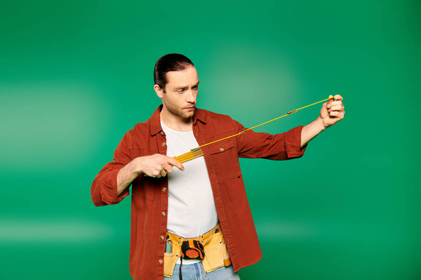 Un hombre con una camisa roja sostiene con confianza una cinta métrica. - Foto, Imagen