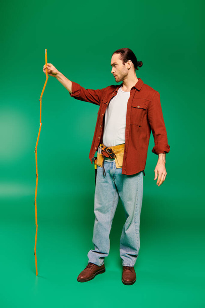 Красивый работник в красной рубашке держит измерительную ленту на зеленом фоне. - Фото, изображение