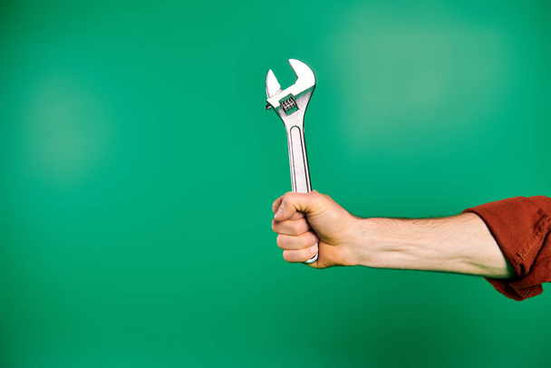 Красивый работник в форме держит гаечный ключ на зеленом фоне. - Фото, изображение